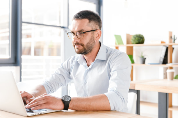 这是一个30多岁的白领在商务中心工作时，穿着白衬衫坐在桌子前使用笔记本电脑的照片图片下载