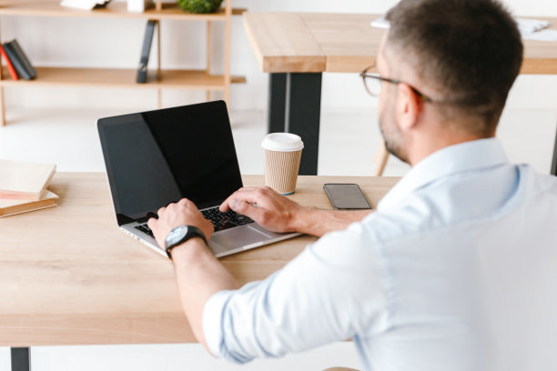 这张照片是一名30多岁的白领在商务中心工作，他穿着白衬衫坐在桌子前，看着黑色的笔记本电脑屏幕图片下载