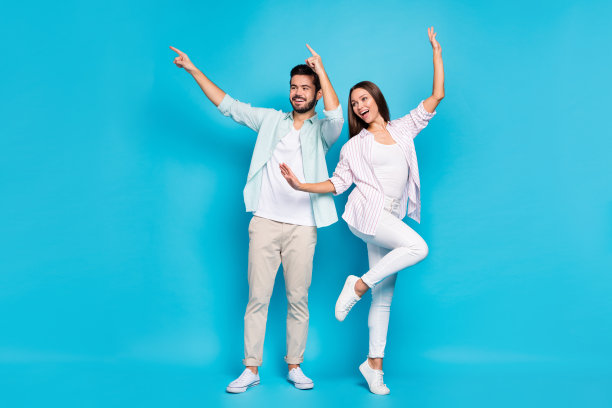 照片甜美有趣的年轻情侣穿着休闲衬衫跳舞指向空荡荡的孤立的蓝色背景图片下载