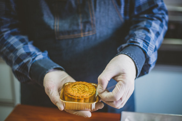 一位亚洲男性面包师把自制的中国月饼放在金色的塑料容器上图片下载