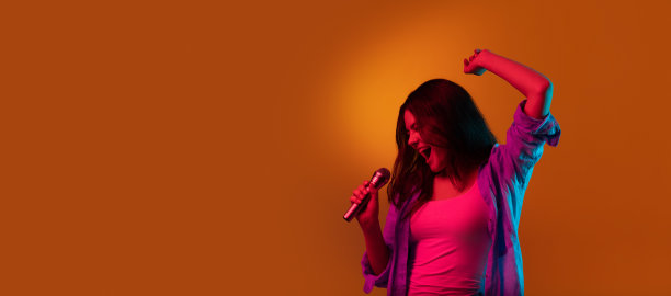 白人女歌手肖像孤立在橙色工作室背景霓虹灯。美丽的女模特在休闲风格与麦克风。人类情感的概念图片下载