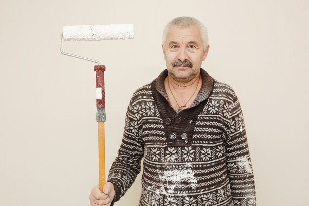 有油漆滚筒的男工人。粉刷公寓，装修用白色油漆。室内装修。图片下载