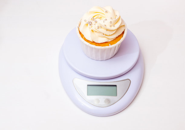 新鲜制作的杯形蛋糕，黄油奶油放在秤上。前视图。白色背景和文字空间。有选择性的重点。图片下载