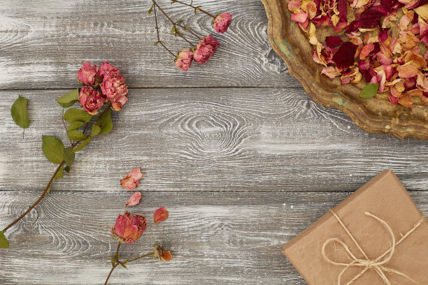 灰色的桌子上放着用牛皮纸包着的礼盒，托盘上放着干枯的玫瑰花瓣。平的样式。为文本复制空间。图片下载