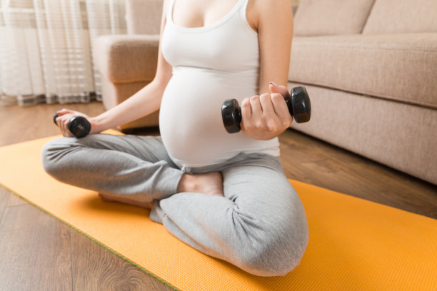 一个怀孕的女孩在一个阳光明媚的日子用哑铃做瑜伽。冠状病毒在家里图片下载
