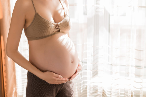 漂亮的年轻孕妇站在家里的窗户旁边图片下载