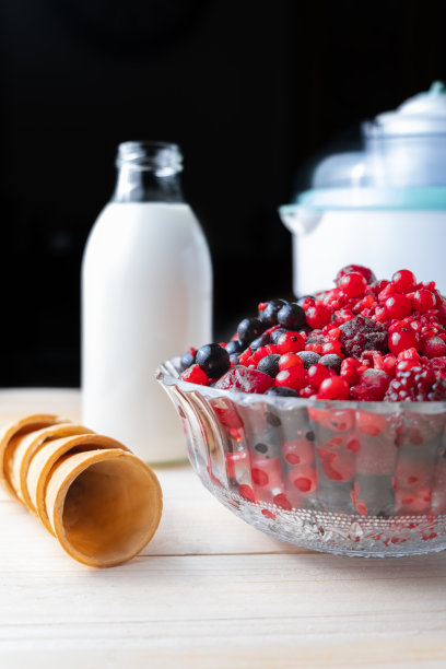 一张木桌的垂直照片，上面有自制冰淇淋的原料:红莓、奶油、冰淇淋机和甜筒图片下载