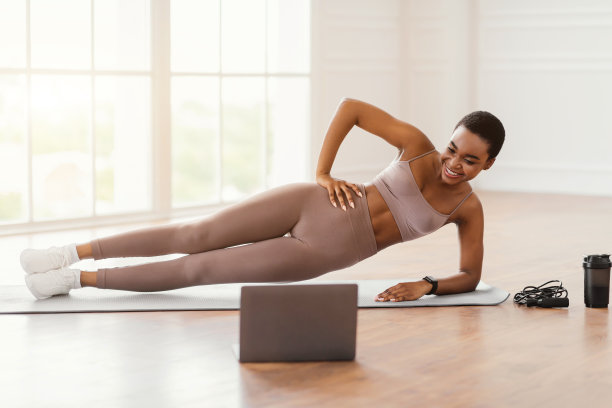 年轻的非洲妇女在垫子上与pc做侧平板支撑图片下载