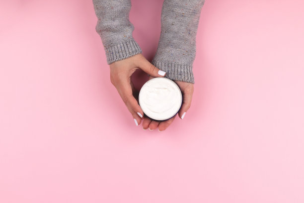 手里拿着粉红色背景上奶油色的罐子图片下载