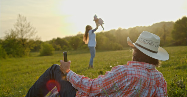 日落时分，牛仔用智能手机和宝宝一起在大自然中远足。春天的居家旅游。图片下载