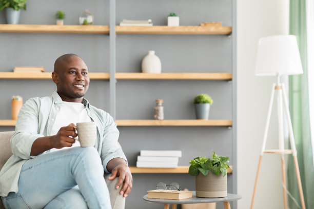 微笑和周到的非裔美国人喝咖啡，坐在扶手椅在客厅内部，自由的空间图片下载