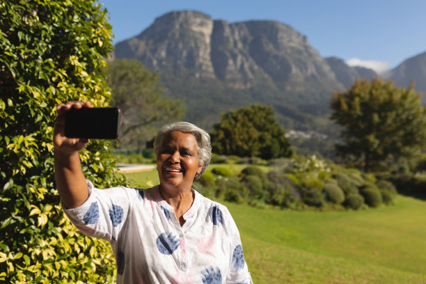 一位非洲裔美国女性在阳光明媚的花园里用智能手机自拍图片下载