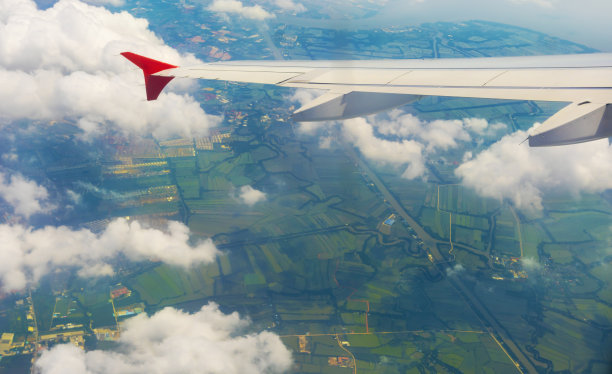 从飞机上看，飞机白色的机翼在清晨飞过云和农田。航空旅行和运输概念。图片下载