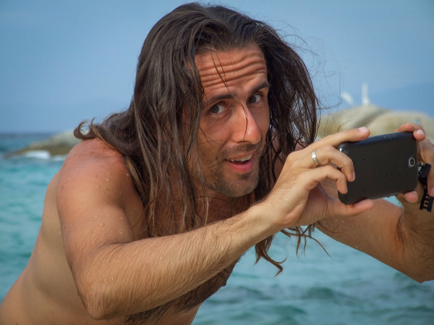 一个迷人的长头发男人在海滩上自拍图片下载