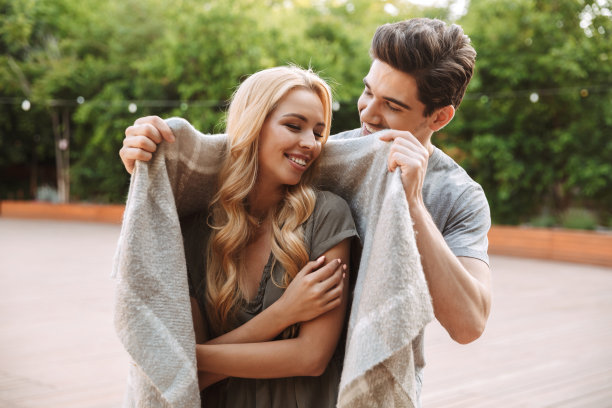 开心的男人把他漂亮的女朋友裹在温暖的毯子里图片下载