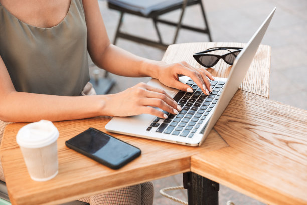 照片中，20多岁的白人女性穿着夏装，在银色笔记本电脑上打字，喝着咖啡，坐在城市咖啡馆或户外餐厅图片下载