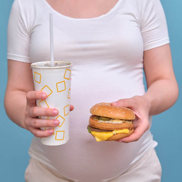 蓝色背景下一个拿着汉堡和苏打水的孕妇，特写图片下载