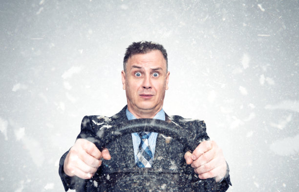 滑稽的情绪受惊吓的人穿着夹克，打着领带，浑身是鸟羽毛，拿着汽车方向盘。灰色背景上飞舞的羽毛。图片下载