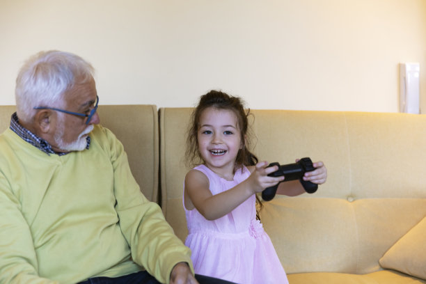 一个快乐的小女孩和她的爷爷在客厅里玩电脑游戏。图片下载