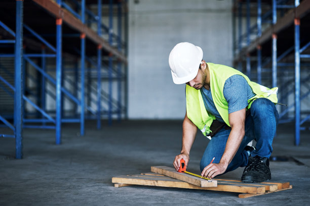 这是一个年轻的建筑工在建筑工地上用卷尺测量的照片图片下载