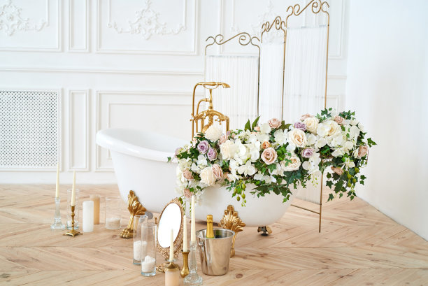 美丽的豪华复古空浴缸与郁郁葱葱的花卉装饰和蜡烛，镜子在浴室内部的地板上，复制空间。独立式白色浴缸，有花，靠近折叠屏风图片下载