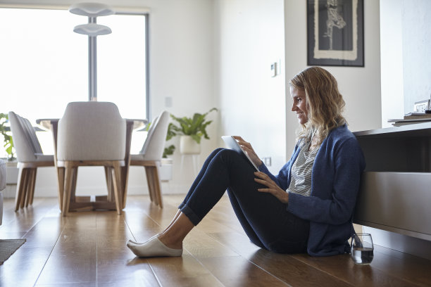 一名愉快的女性坐在家里的地板上用数码设备进行视频通话的侧面画面图片下载