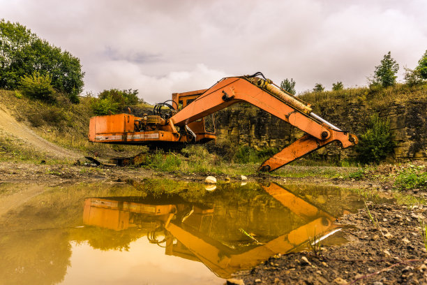 废弃的橙色挖掘机在泥泞的水坑中反射图片下载