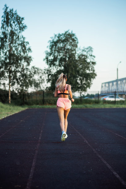 运动女孩在跑道上奔跑从后面看体育场图片下载
