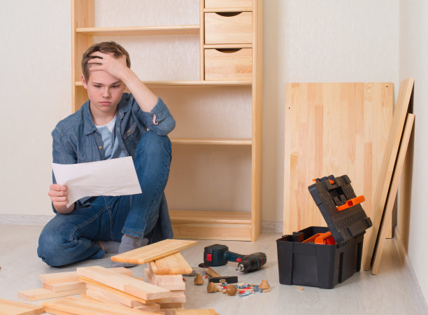 一个年轻人在家里组装家具。青少年试图阅读与问题和困难的diy指导。图片下载