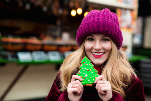 快乐的年轻女子拿着甜蜜的圣诞姜饼，在灯光装饰的背景上摆姿势图片下载