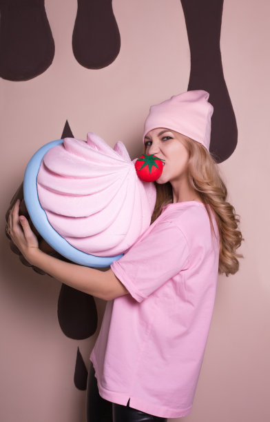 快乐的金发女人，粉红t恤和帽子咬大蛋糕图片下载