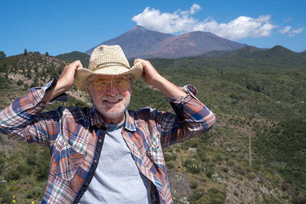 有魅力的白胡子老人在户外游览山景，微笑着看着相机。背景是艾尔泰德火山。图片下载
