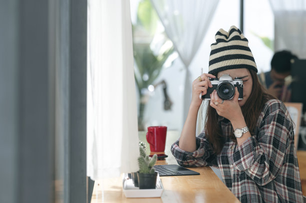 年轻的女摄影师坐在咖啡馆里用胶卷相机拍照。图片下载