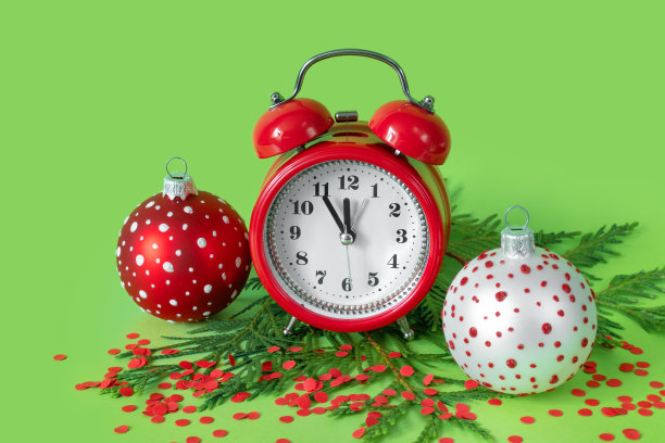 绿色背景上的红白色圣诞球、彩纸屑、闹钟和树枝，新年倒计时5分钟图片下载