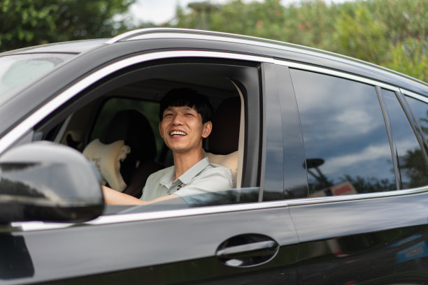 在停车场里，一名亚洲男性司机坐在驾驶座上，脸上带着微笑图片下载