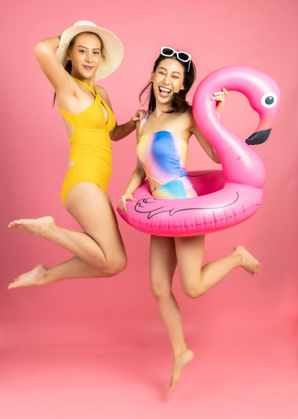 美丽性感的亚洲女人在比基尼和微笑站在粉红色的背景孤立。暑假快乐的旅行概念。图片下载