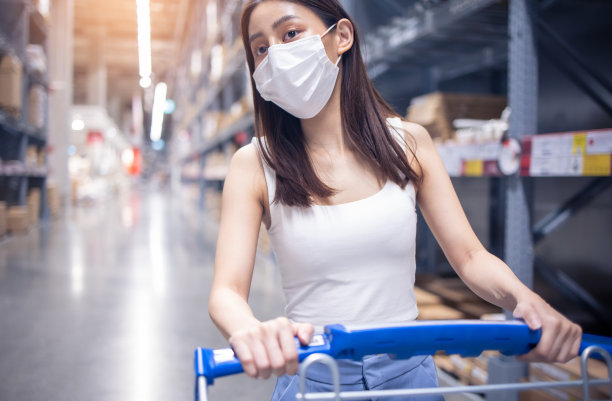 2019冠状病毒(covid-19)大流行期间，年轻的亚洲女性戴着医用口罩在仓库购物。图片下载