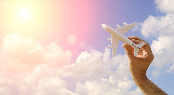 在蓝天旗帜背景上飞行的飞机。手里拿着一架玩具飞机飞着去旅行。夏季，假期，旅游，放松，旅游和航班的概念。图片下载