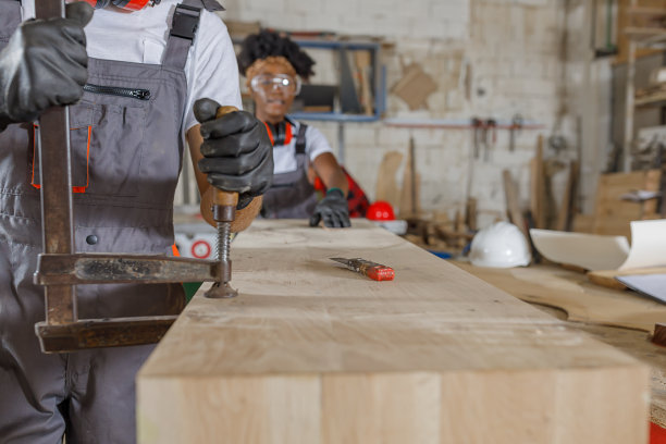 一个有经验的木匠和他的女非洲同事正在使用一个钳，而工作在一个大车间。图片下载