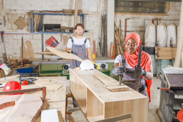一位经验丰富的木匠和他的女穆斯林同事在一个大车间工作时使用夹具。图片下载
