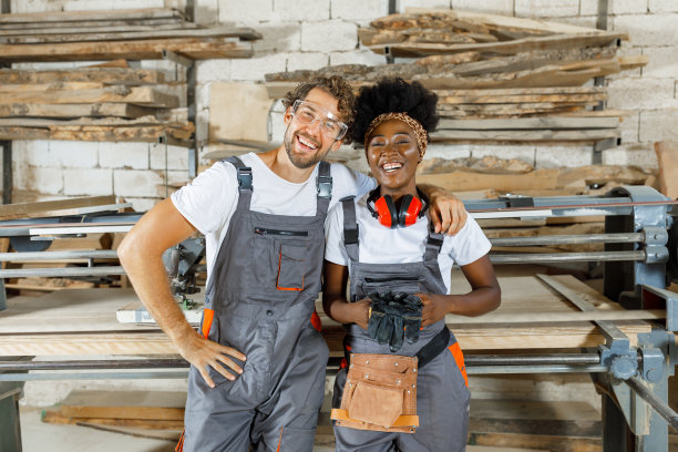 一对满意的多文化木匠在一个宽敞的车间里对着镜头微笑。图片下载