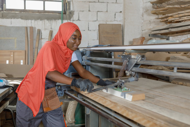 一名穆斯林妇女在木工制造的机器上打磨木头的照片。图片下载