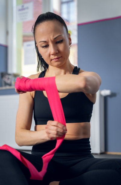 一个严肃的亚洲女人的垂直照片，在健身房，集中应用粉红色踢拳击带。图片下载