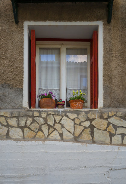 希腊阿拉科瓦市一幢漂亮的房子的窗户，有花边窗帘、鲜花和红色百叶窗图片下载