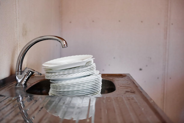 在肮脏的厨房里，水龙头下面的金属水槽里放着一大堆肮脏的瓷器盘子。图片下载