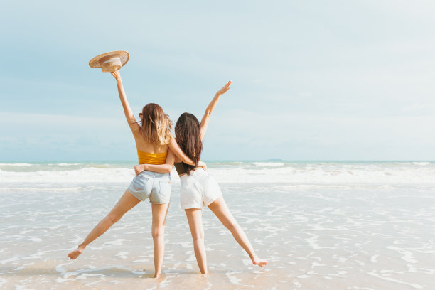 两名亚洲妇女在热带国家度假时，穿着夏季休闲装在海边玩耍。夏日里，年轻美丽的女子在海滩上愉快地跳舞图片下载