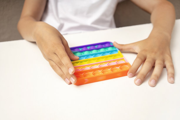 匿名儿童与多彩的poppit游戏。少年的手玩着五颜六色的pop它坐立不安的玩具。简单的酒窝游戏图片下载