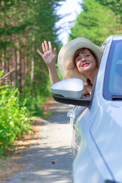 在一个阳光明媚的夏日里，一个美丽的年轻女子在森林道路上看着窗外的绿树图片下载