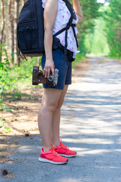 在一个阳光明媚的夏日里，一个背着背包和相机的女游客在森林里的绿树映衬下行走图片下载