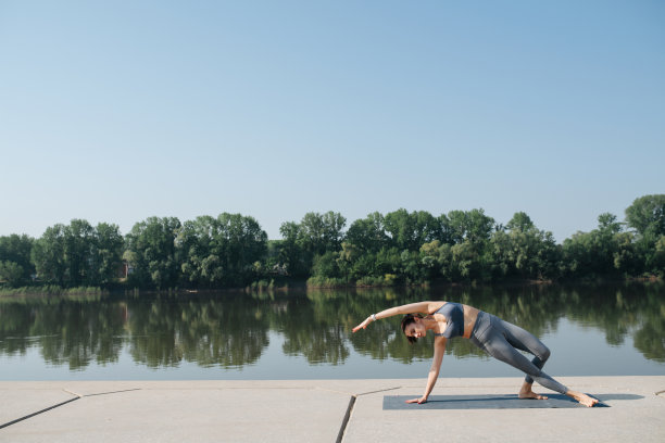 美丽的黑发女子做瑜伽在一个风景优美的地点在河边图片下载